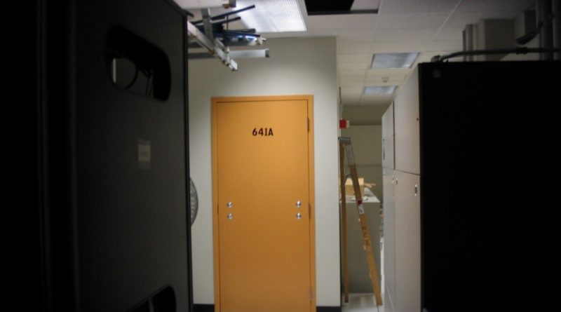 a photo of the exterior of Room 641A, which has a yellow door without a door handle, in a dimly lit datacenter in a San Francisco AT&T hub.
